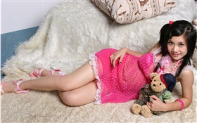 微笑粉红色连衣裙的亚洲女孩，床，玩具 高清壁纸